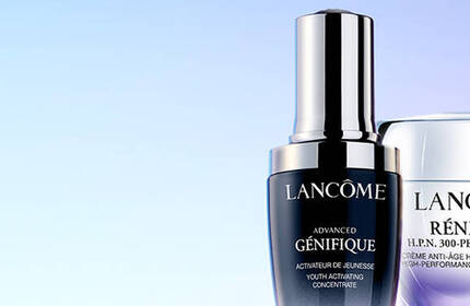 Three skincare products from Lancome displayed against a gradient background. The bottles include Advanced Genifique serum, Renergie Multi-Lift Ultra cream, and Absolue Soft Cream.