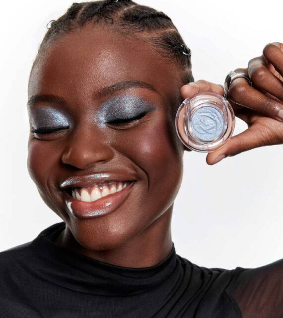 Femme souriante avec un fard a paupieres bleu scintillant tenant un fard a paupieres mono assorti.