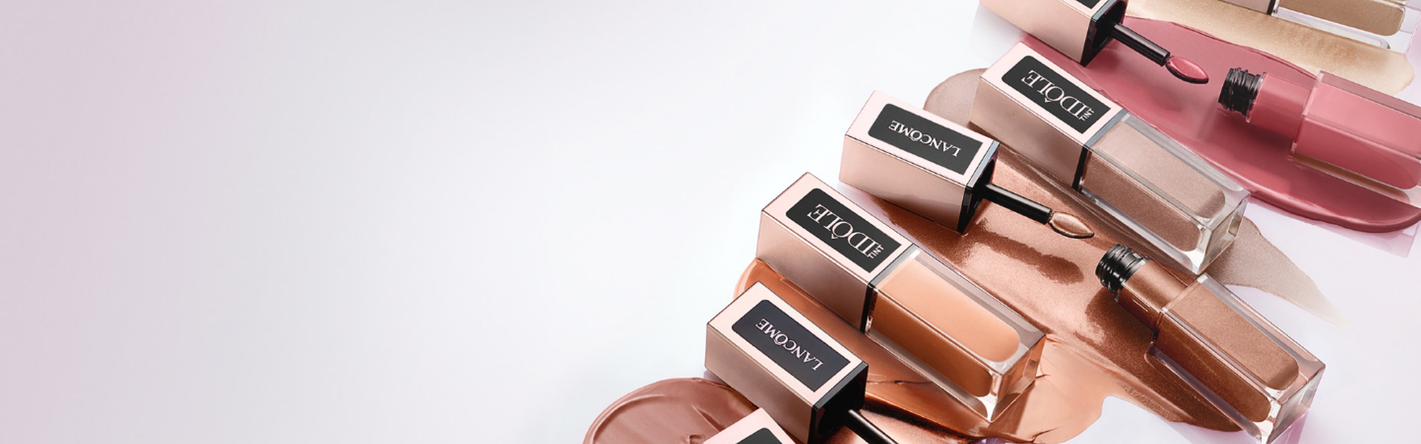 Flacons de maquillage Lancôme en teintes variées, disposés artistiquement sur une surface lisse, avec des coulures de produit.