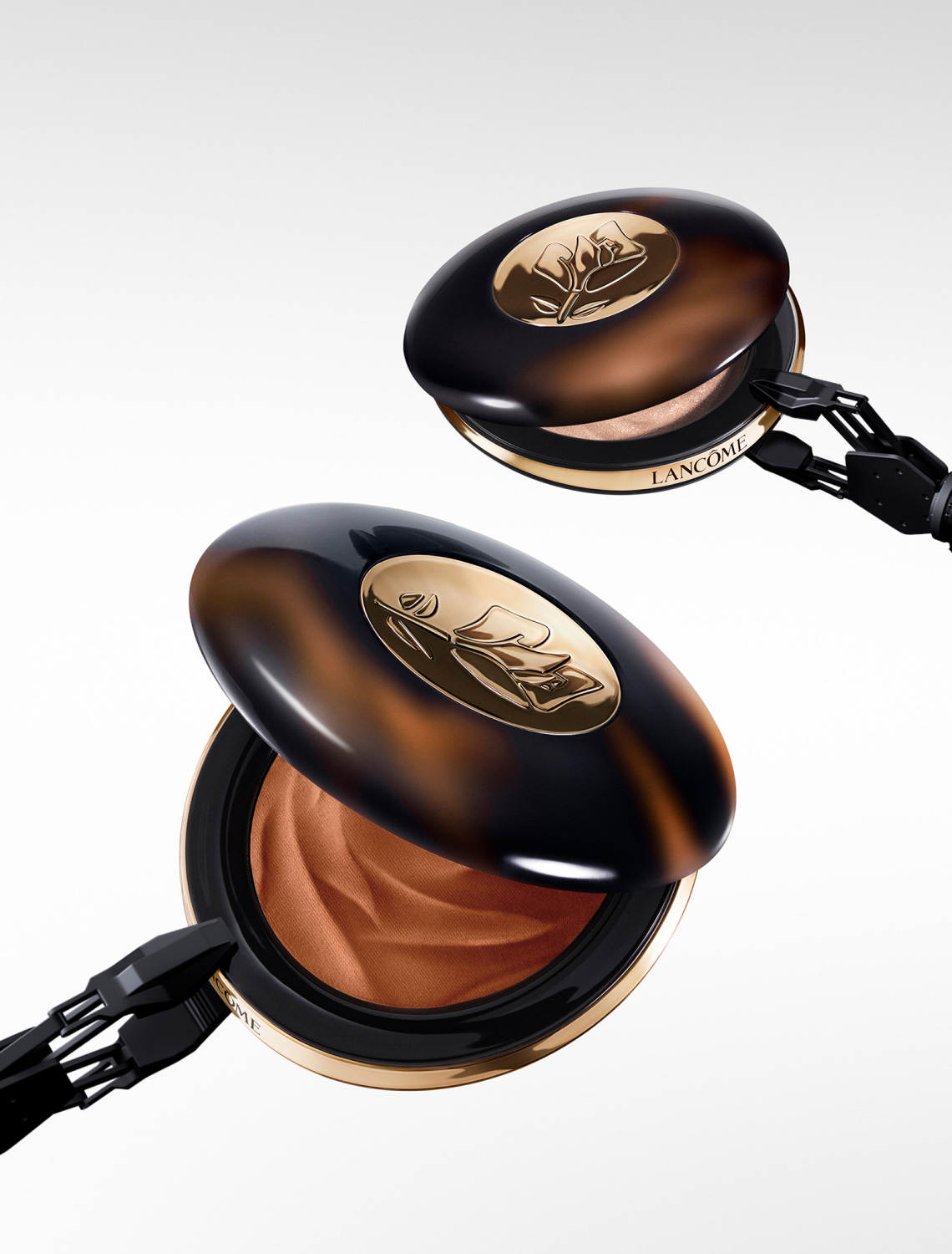 Boîtier de fond de teint Lancôme, élégant, en forme de coquillage avec un motif de fleur, ouvert pour révéler la couleur bronzée.